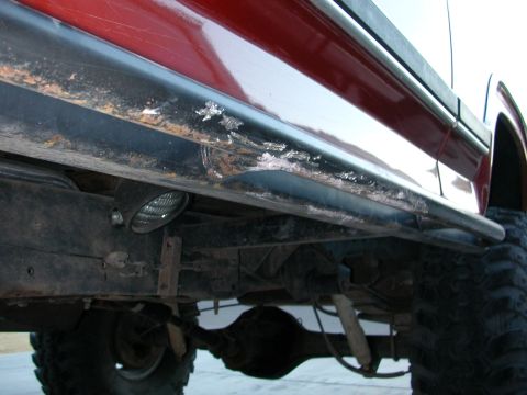 1984 Ford Bronco - Close-up view of the lower side panel and undercarriage of a 1984 Ford Bronco, showing rust and a mounted spotlight.