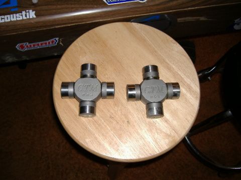 1979 Ford Bronco - Two CTM U-joints are displayed on a wooden stool, with various stickers visible on a surface in the background.