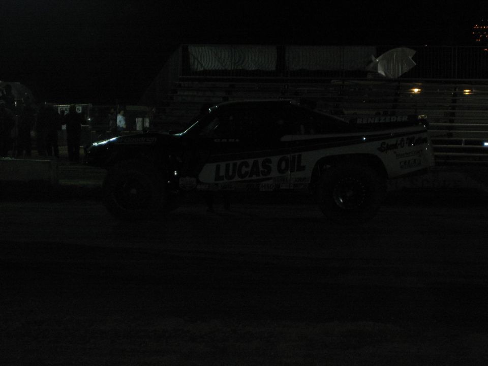 Dark night photo of a Lucas Oil-branded off-road truck on a dirt track by empty grandstands