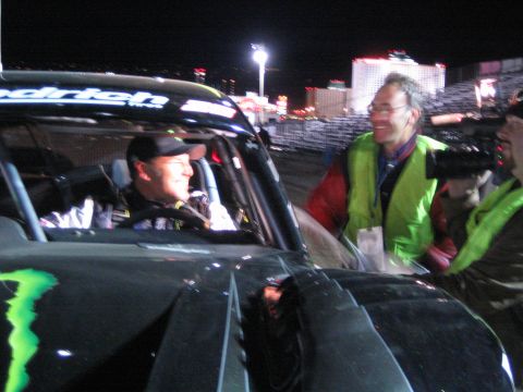 1990 Ford Bronco - driver sits in a Monster Energy-graphic off-road truck at night, chatting with a smiling official in a yellow safety vest.