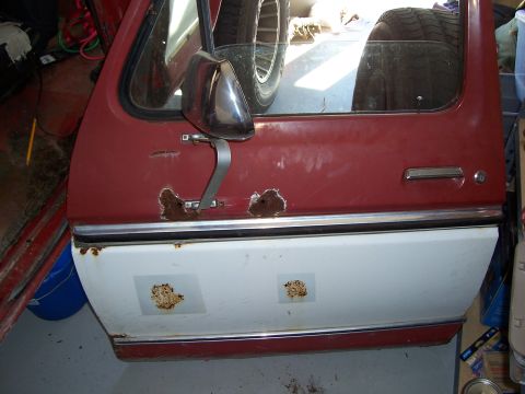 1978 Ford Bronco - A red and white vehicle door with visible rust damage and chrome trim is shown.