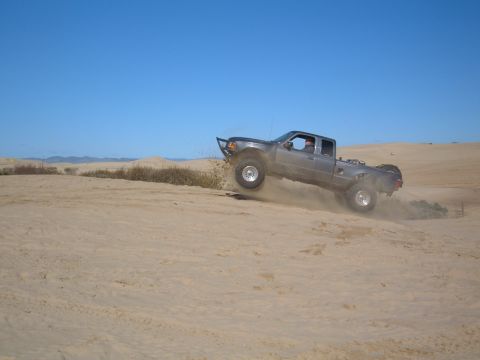 1985 Ford Ranger - A gray Ford Ranger is airborne while cresting a sand dune under a clear blue sky.