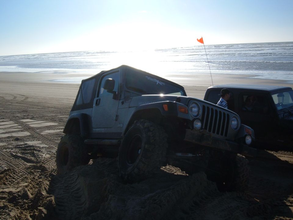 Jeep Wrangler with soft top on a sand dune, another dark SUV behind it