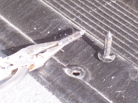 1978 Ford Bronco - A pair of pliers is used to remove a plastic fastener from a textured surface, possibly interior trim.
