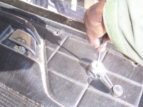 1978 Ford Bronco - A hand uses a screwdriver to remove the window crank from a vehicle's interior door panel.