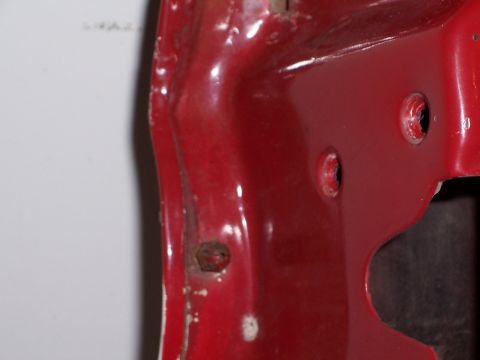 1978 Ford Bronco - A close-up view of a red painted metal surface with visible bolt holes and some surface imperfections.