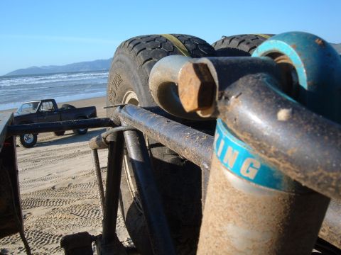1985 Ford Ranger - A view of off-road suspension components and a spare tire, with a pickup truck on the beach in the distance.