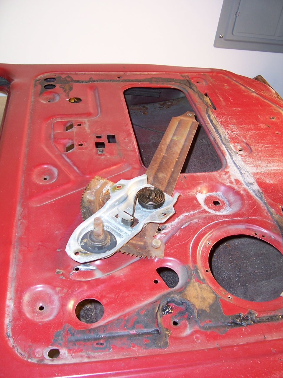 Red car door interior showing window regulator mechanism and rust damage
