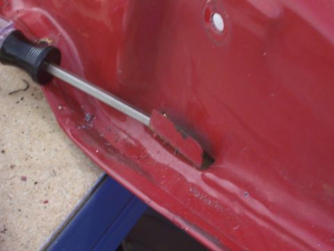 1978 Ford Bronco - A screwdriver is being used to pry open a section of a red car door's interior panel.
