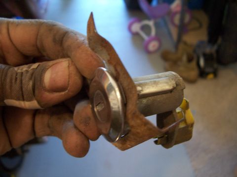 1978 Ford Bronco - A dirty hand holds a rusty ignition lock cylinder, showing the keyhole and surrounding metal components.