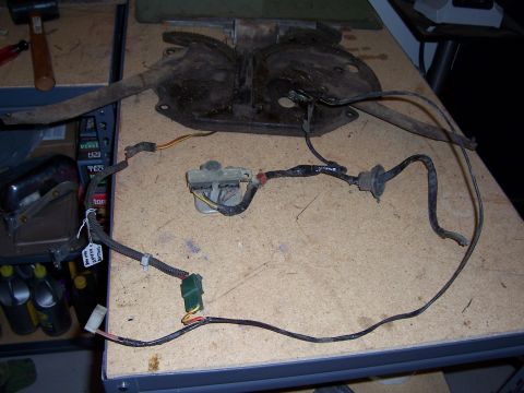 1978 Ford Bronco - A greasy tailgate window regulator with twin toothed sector gears sits on a particleboard workbench alongside its removed wiring harness, r…