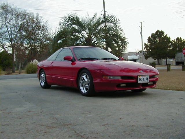 Red coupe parked on concrete driveway, front 3/4 view. License plate JX-8794 is visible