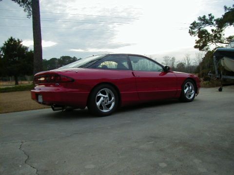 1997 Ford Probe - A red coupe with a black roof is parked on a concrete driveway next to a boat on a trailer.