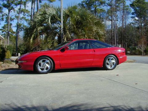 1997 Ford Probe - A red 1997 Ford Probe is parked on a concrete surface with trees in the background.