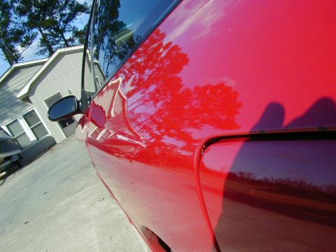 1997 Ford Probe - A red car's side panel reflects trees and a house under a blue sky.