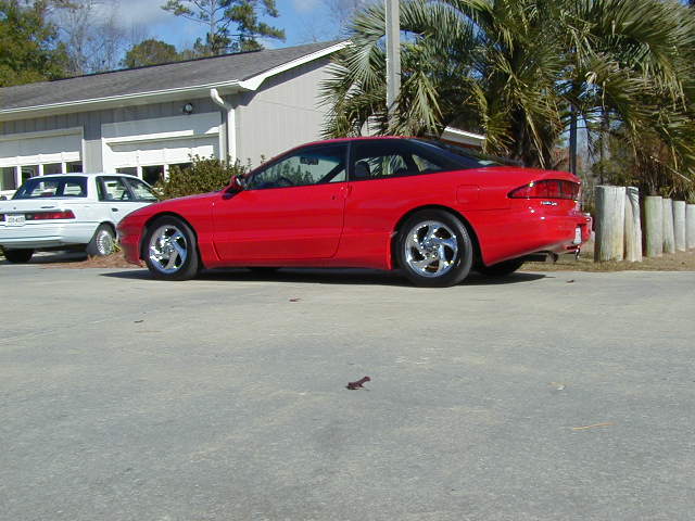 Red 1997 Ford Probe parked next to a white car. The Probe has a black roof and aftermarket wheels