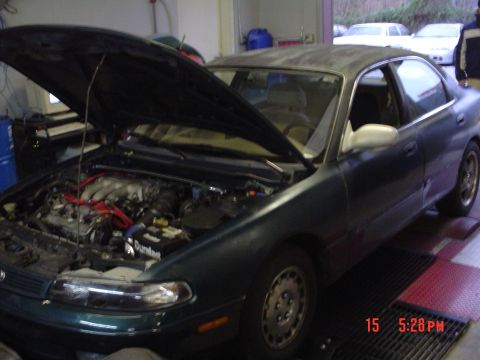 1994 Mazda 626 - Dark green sedan with hood open, revealing the engine bay and some aftermarket modifications.