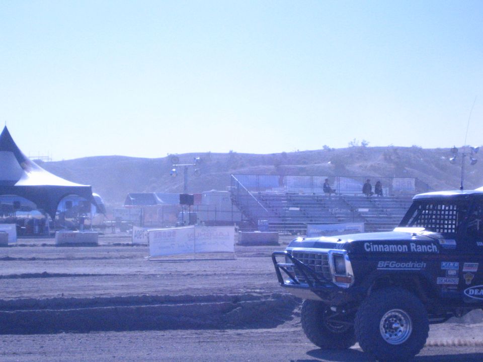 Blue Cinnamon Ranch race truck front three-quarter on dirt with tent and grandstands