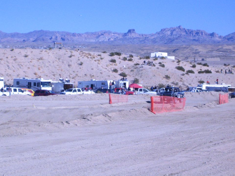 Desert staging area with parked RVs, trucks and orange fence below jagged mountains