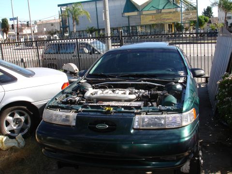1993 Ford Taurus - 1993 Ford Taurus with its hood open, parked next to another vehicle.