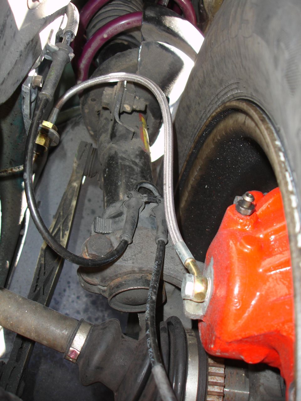 Car suspension strut with purple spring, brake caliper, and tire. Close-up view of automotive parts