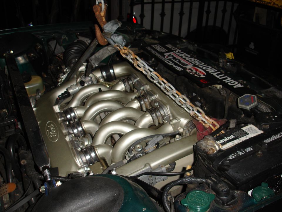 Ford SHO V6 with curved tubular intake runners and a hoist chain rigged for engine removal