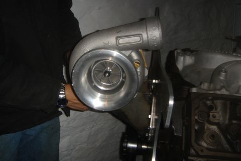 1969 Ford Mustang - A turbocharger is being held up to an engine block, likely for installation or inspection.