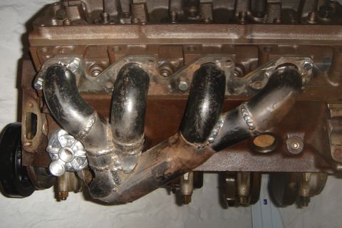 1969 Ford Mustang - Close-up of an engine block with custom exhaust headers, showing welded pipes and a pulley wheel.