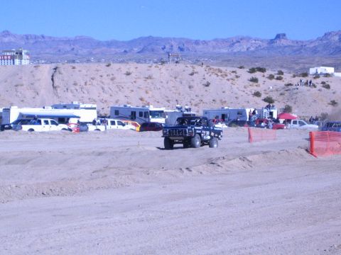 1990 Ford Bronco - black lifted off-road vehicle drives the desert dirt course with an RV camp and rugged mountains in the background.