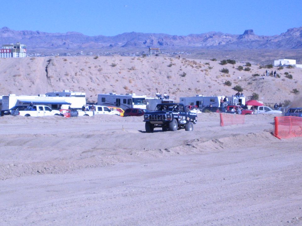 Black lifted off-road vehicle on desert dirt course with RV camp and mountains behind