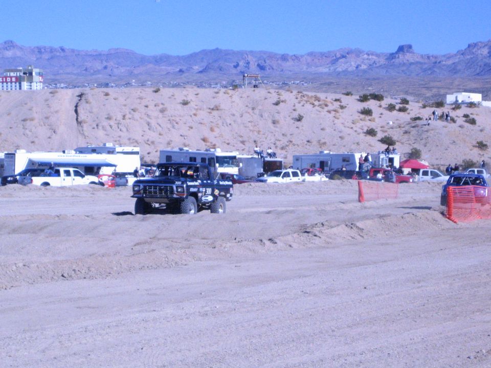 Dark off-road truck on dirt course with RV pits and desert mountain range