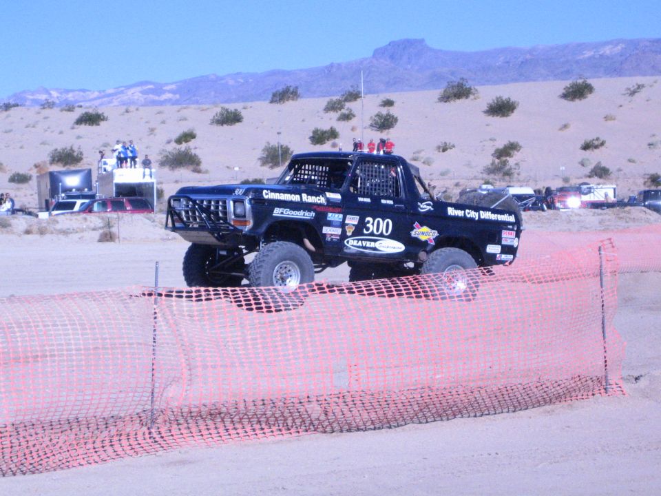 Black Ford race truck number 300 driving past orange fence in the desert