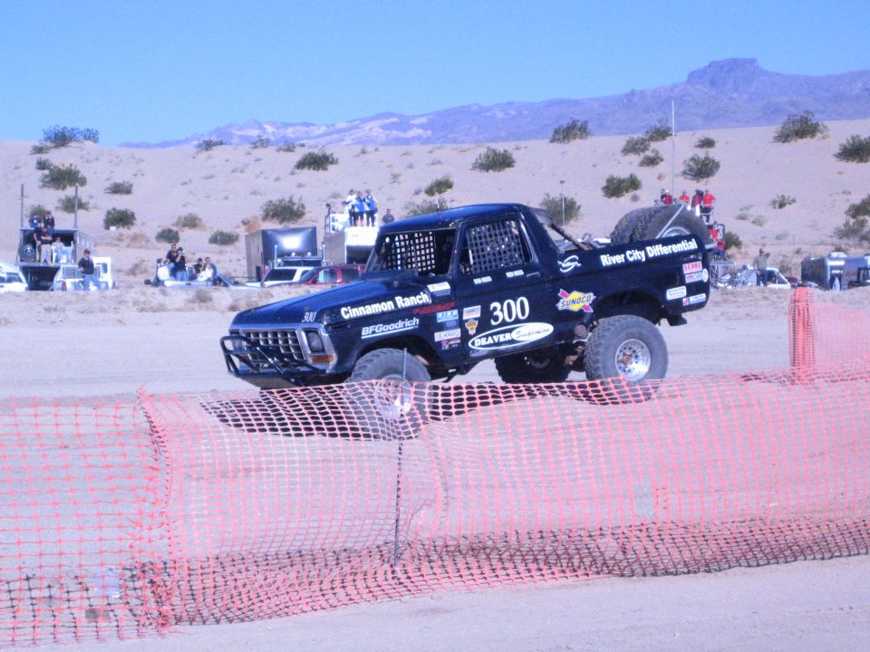 Side view of black Ford race truck 300 with sponsor decals behind fencing