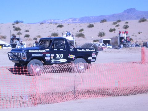 1990 Ford Bronco - Profile of black Ford race truck number 300 bearing River City Differential and other sponsor decals on a dirt course.