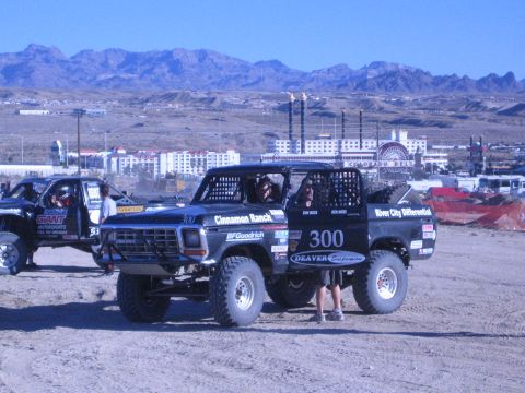 1990 Ford Bronco - Black Ford race truck number 300 parked on dirt with casino hotels and rugged mountains in the background.