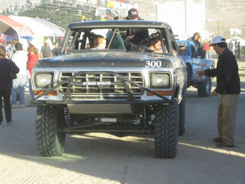1990 Ford Bronco - Front view of black Ford race truck number 300 with crew and spectators gathered in a busy pit area.