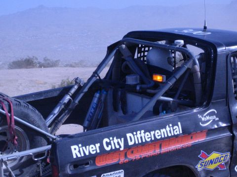 1990 Ford Bronco - exposed roll cage, shocks and "River City Differential" decals of a black race truck overlook a hazy desert valley.