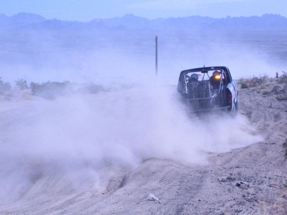Off-road race truck driving away into a haze of dust in the desert