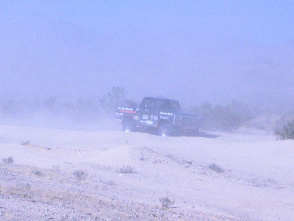 Off-road race truck numbered 300 partly obscured by desert dust