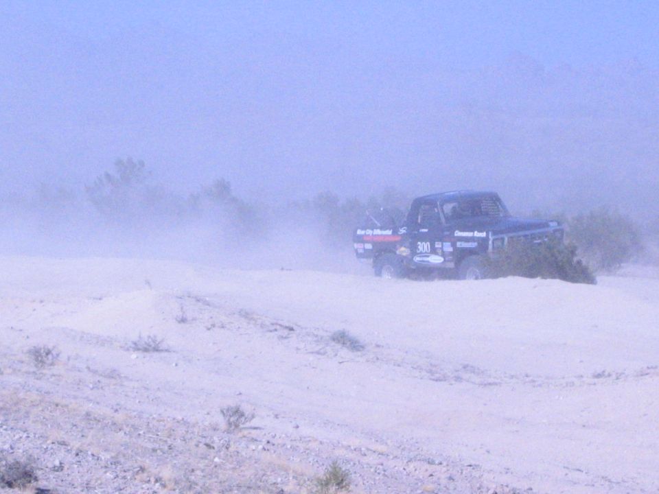 Black race truck 300 driving past desert brush in a dust haze