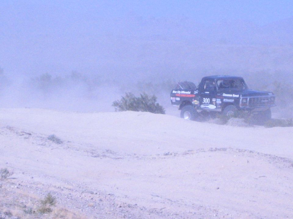 Off-road race truck 300 cresting a sandy berm in the desert