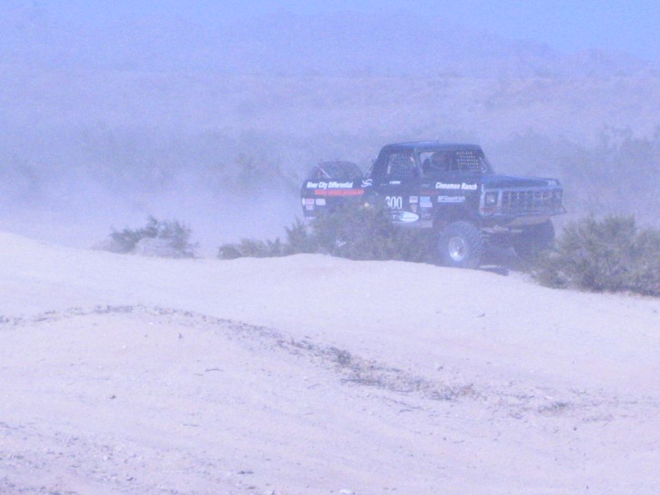 Black race truck 300 driving across a sandy desert ridge