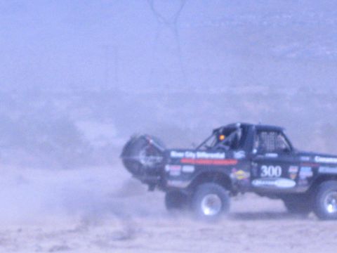 1990 Ford Bronco - off-road race truck numbered 300 lifts its front end while powering through a dusty desert section.
