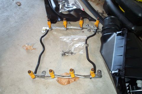 1998 Ford Crown Victoria - A fuel injector rail with yellow injectors and an air intake box are laid out on a concrete floor.