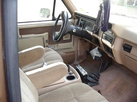 1985 Ford Bronco - The interior of a truck shows tan seats, a steering wheel, and a dashboard with a radio and gear shifter.