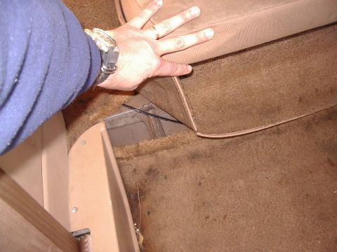 1985 Ford Bronco - A hand lifts the carpet to expose a metal channel beneath the seat base.