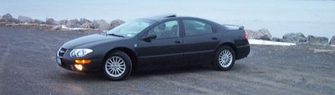 1999 Chrysler 300M - A black 1999 Chrysler 300M sits parked on a gravel lot by the water.