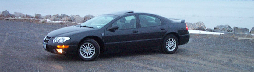 Black Chrysler 300M sedan side profile on gravel lot by rocky waterfront at dusk