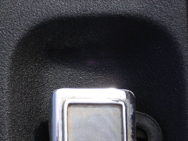 Close-up of worn chrome rectangular handle bezel on black textured panel