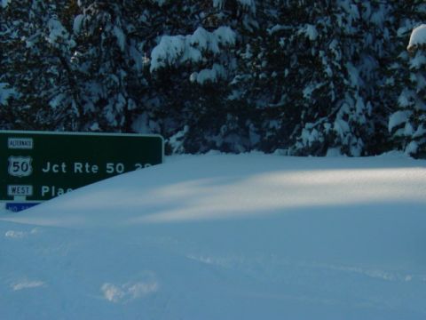 1986 Ford Bronco - A snow-covered landscape features a green road sign indicating Jct Rte 50 West, with snow-laden trees in the background.